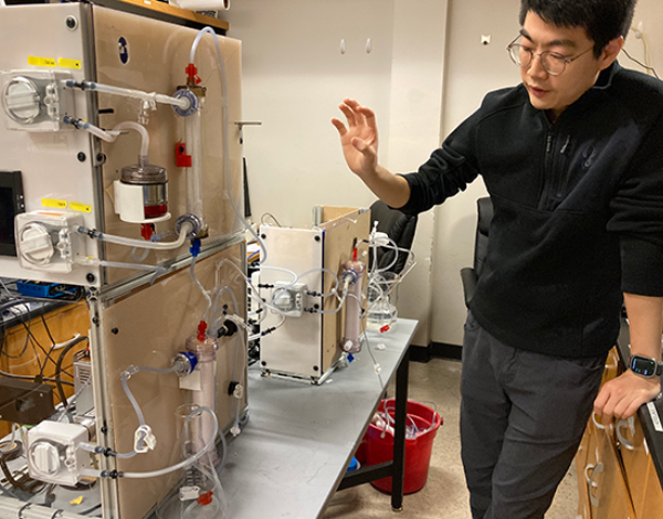 UW Mechanical Engineering grad student Shaohang Hao stands in front of medical device with attached bottles and tubes